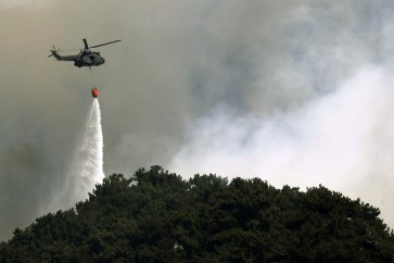 A Lebanese army helicopter drops water on a forest fire in the Qubayyat area of northern Lebanon's remote Akkar region on July 29, 2021. - A Lebanese teenager was killed as he joined volunteers battling devastating forest wildfires in northern Lebanon, where firefighters were struggling to protect homes from the blaze. (Photo by JOSEPH EID / AFP)