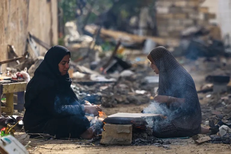 فلسطينيتان تخبزان على نار الحطب أمام منزليهما المدمرين (الفرنسية)